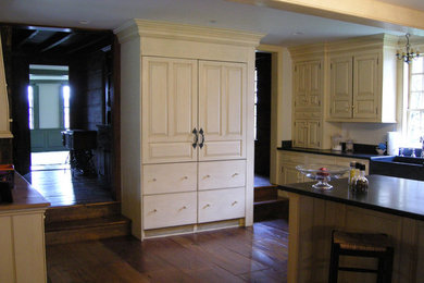 Modelo de cocinas en L grande con despensa, fregadero de doble seno, puertas de armario blancas, salpicadero blanco, suelo de madera en tonos medios y una isla