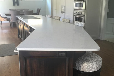 Example of a large classic medium tone wood floor eat-in kitchen design in Chicago with recessed-panel cabinets, white cabinets, solid surface countertops, stainless steel appliances and an island