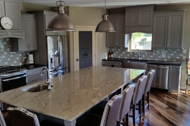 Large transitional l-shaped painted wood floor eat-in kitchen photo in Other with a farmhouse sink, shaker cabinets, gray cabinets, solid surface countertops, multicolored backsplash, ceramic backsplash, stainless steel appliances and an island