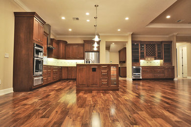 Immagine di una cucina classica di medie dimensioni con lavello sottopiano, ante con bugna sagomata, ante in legno bruno, top in granito, paraspruzzi bianco e elettrodomestici in acciaio inossidabile