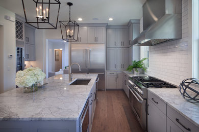 Inspiration for a mid-sized transitional l-shaped medium tone wood floor open concept kitchen remodel in Orlando with an undermount sink, recessed-panel cabinets, gray cabinets, granite countertops, white backsplash, ceramic backsplash, stainless steel appliances and an island