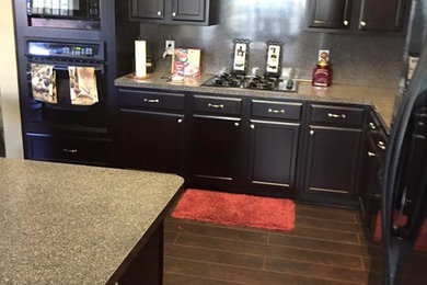 Example of a mid-sized classic l-shaped medium tone wood floor enclosed kitchen design in Houston with recessed-panel cabinets, black cabinets, laminate countertops, gray backsplash, stone slab backsplash, black appliances and an island