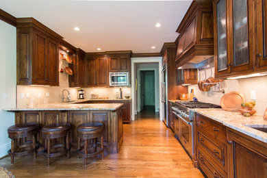 Example of a classic kitchen design in Other with dark wood cabinets, granite countertops, beige backsplash, stainless steel appliances and a peninsula