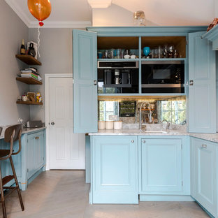 Photo of a small traditional kitchen/diner in London with a submerged sink, raised-panel cabinets, blue cabinets, marble worktops, grey splashback, marble splashback, black appliances, light hardwood flooring, a breakfast bar, beige floors and grey worktops.