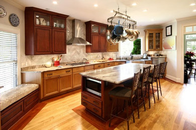 Kitchen - large transitional light wood floor and brown floor kitchen idea in Raleigh with a farmhouse sink, raised-panel cabinets, medium tone wood cabinets, granite countertops, gray backsplash, marble backsplash, stainless steel appliances, an island and beige countertops