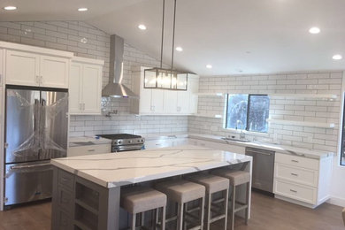 Large classic l-shaped kitchen/diner in Los Angeles with a single-bowl sink, shaker cabinets, white cabinets, marble worktops, white splashback, metro tiled splashback, stainless steel appliances, medium hardwood flooring, an island and brown floors.