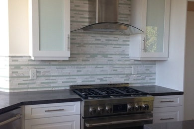 Photo of a medium sized traditional l-shaped kitchen/diner in Los Angeles with white cabinets, composite countertops, multi-coloured splashback, stainless steel appliances, an island, travertine flooring, marble splashback and recessed-panel cabinets.