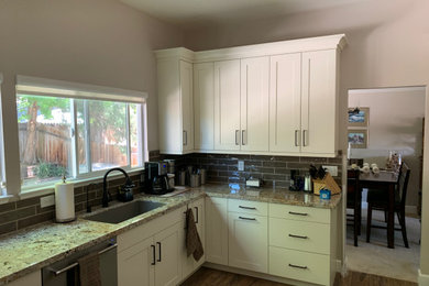 Example of a mid-sized transitional l-shaped laminate floor and brown floor eat-in kitchen design in Other with an undermount sink, shaker cabinets, white cabinets, granite countertops, brown backsplash, ceramic backsplash, stainless steel appliances, no island and brown countertops