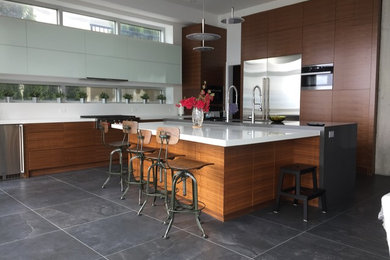 Large modern l-shaped kitchen in Vancouver with a submerged sink, flat-panel cabinets, medium wood cabinets, engineered stone countertops, white splashback, glass sheet splashback, stainless steel appliances, an island and grey floors.