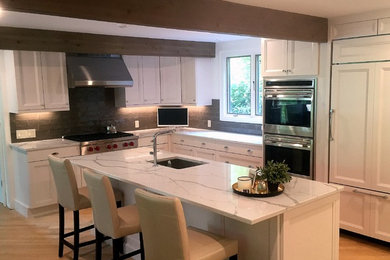 Inspiration for a mid-sized transitional l-shaped light wood floor and brown floor enclosed kitchen remodel in Boston with an undermount sink, recessed-panel cabinets, white cabinets, quartzite countertops, gray backsplash, glass tile backsplash, an island, paneled appliances and white countertops