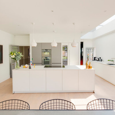 Large trendy beige floor eat-in kitchen photo in London with an undermount sink, flat-panel cabinets, white cabinets, stainless steel appliances, an island and white countertops