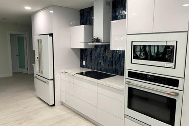 Inspiration for a small modern galley kitchen remodel in Miami with an undermount sink, flat-panel cabinets, white cabinets, quartz countertops, blue backsplash, glass tile backsplash, white appliances and white countertops
