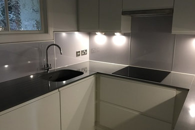 This is an example of a small contemporary u-shaped enclosed kitchen in Edinburgh with an integrated sink, flat-panel cabinets, white cabinets, engineered stone countertops, metallic splashback and vinyl flooring.