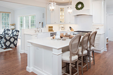 Inspiration for a mid-sized transitional l-shaped medium tone wood floor and brown floor eat-in kitchen remodel in New York with a farmhouse sink, recessed-panel cabinets, white cabinets, quartzite countertops, white backsplash, subway tile backsplash, stainless steel appliances, an island and white countertops