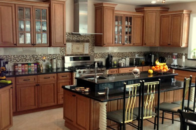 Large elegant l-shaped eat-in kitchen photo in New York with an undermount sink, raised-panel cabinets, medium tone wood cabinets, granite countertops, beige backsplash, ceramic backsplash, stainless steel appliances and an island