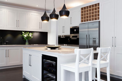 Large contemporary galley kitchen/diner in London with a double-bowl sink, flat-panel cabinets, white cabinets, granite worktops, black splashback, glass sheet splashback, stainless steel appliances, dark hardwood flooring and an island.
