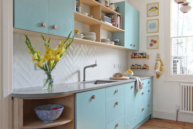 Idéer för små skandinaviska linjära kök, med en undermonterad diskho, släta luckor, blå skåp, vitt stänkskydd, mellanmörkt trägolv och bänkskiva i betong