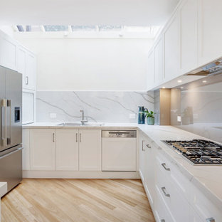 Photo of a mid-sized transitional l-shaped kitchen in Sydney with a drop-in sink, shaker cabinets, white cabinets, grey splashback, glass sheet splashback, stainless steel appliances, beige floor and grey benchtop.