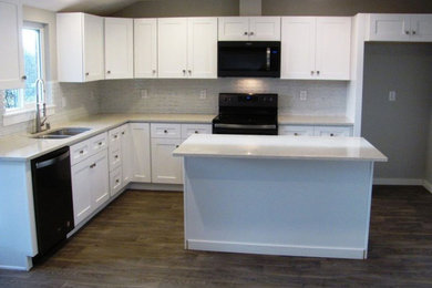 Mid-sized transitional l-shaped medium tone wood floor and gray floor eat-in kitchen photo in Portland with an undermount sink, shaker cabinets, white cabinets, quartz countertops, white backsplash, glass sheet backsplash, black appliances, an island and white countertops