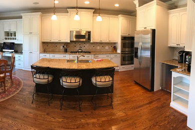 Inspiration for a large timeless l-shaped medium tone wood floor eat-in kitchen remodel in Raleigh with a single-bowl sink, raised-panel cabinets, white cabinets, granite countertops, beige backsplash, travertine backsplash, stainless steel appliances and an island