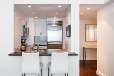 Eat-in kitchen - small contemporary u-shaped dark wood floor eat-in kitchen idea in New York with an undermount sink, recessed-panel cabinets, white cabinets, solid surface countertops, white backsplash, subway tile backsplash, stainless steel appliances and no island