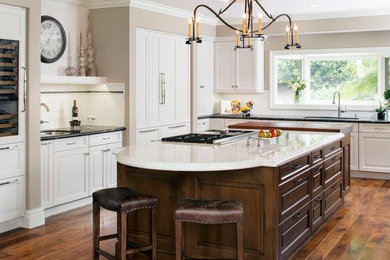 Inspiration for a large transitional l-shaped dark wood floor kitchen pantry remodel in Orange County with a double-bowl sink, flat-panel cabinets, white cabinets, granite countertops, white backsplash, subway tile backsplash, stainless steel appliances and an island