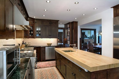 Mid-sized trendy l-shaped ceramic tile eat-in kitchen photo in Detroit with a drop-in sink, raised-panel cabinets, dark wood cabinets, wood countertops, white backsplash, ceramic backsplash, stainless steel appliances and an island