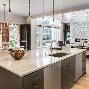 Contemporary kitchen in Sussex with a submerged sink, flat-panel cabinets, grey cabinets, stainless steel appliances, medium hardwood flooring, an island, brown floors and beige worktops.