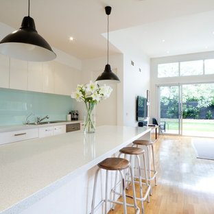 Inspiration for a contemporary single-wall open plan kitchen in Sussex with flat-panel cabinets, white cabinets, blue splashback, medium hardwood flooring, an island, brown floors and white worktops.