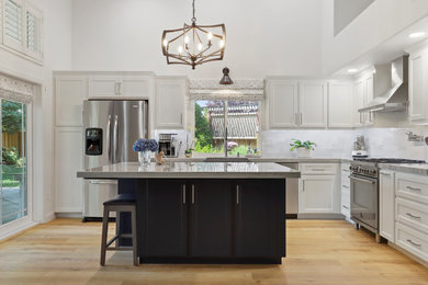 Eat-in kitchen - contemporary brown floor eat-in kitchen idea in San Francisco with a farmhouse sink, shaker cabinets, white cabinets, quartzite countertops, white backsplash, ceramic backsplash, stainless steel appliances, an island and white countertops