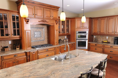 Example of a large classic medium tone wood floor kitchen design in DC Metro with a double-bowl sink, raised-panel cabinets, medium tone wood cabinets, granite countertops, beige backsplash, ceramic backsplash, stainless steel appliances and an island