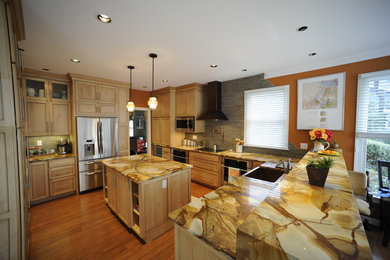 Example of a mid-sized transitional u-shaped light wood floor eat-in kitchen design in Baltimore with a farmhouse sink, light wood cabinets, onyx countertops, stainless steel appliances, an island and beaded inset cabinets