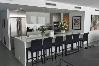Example of a huge trendy galley concrete floor eat-in kitchen design in Chicago with an undermount sink, flat-panel cabinets, white cabinets, quartz countertops, white backsplash, stone slab backsplash, stainless steel appliances and an island