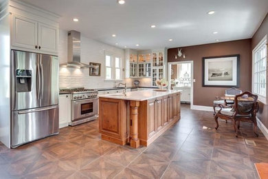 Inspiration for a large transitional l-shaped porcelain tile eat-in kitchen remodel in DC Metro with white cabinets, white backsplash, ceramic backsplash, stainless steel appliances, an island, an undermount sink, raised-panel cabinets and marble countertops