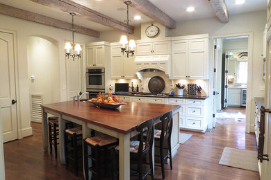 Example of a mid-sized arts and crafts single-wall dark wood floor eat-in kitchen design in Birmingham with an undermount sink, recessed-panel cabinets, white cabinets, wood countertops, paneled appliances and an island