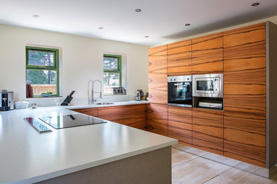 Photo of a medium sized contemporary u-shaped open plan kitchen in West Midlands with an integrated sink, flat-panel cabinets, light wood cabinets, glass worktops, integrated appliances and porcelain flooring.