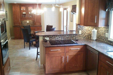 Example of a mid-sized u-shaped limestone floor eat-in kitchen design in Bridgeport with medium tone wood cabinets, granite countertops, mosaic tile backsplash, stainless steel appliances and no island
