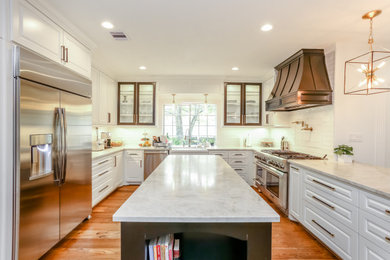 Example of a large transitional u-shaped medium tone wood floor and brown floor enclosed kitchen design in Houston with a farmhouse sink, raised-panel cabinets, white cabinets, granite countertops, white backsplash, glass tile backsplash, stainless steel appliances, an island and white countertops