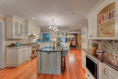 Example of a large u-shaped medium tone wood floor eat-in kitchen design in Other with an undermount sink, raised-panel cabinets, white cabinets, granite countertops, multicolored backsplash, glass tile backsplash, stainless steel appliances and an island