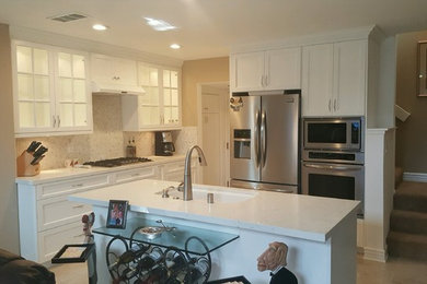 This is an example of a large classic u-shaped kitchen/diner in Orange County with a submerged sink, recessed-panel cabinets, white cabinets, engineered stone countertops, white splashback, mosaic tiled splashback, stainless steel appliances, porcelain flooring, an island, beige floors and white worktops.