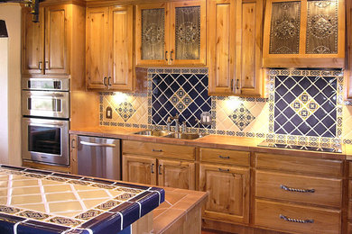 ポートランドにある中くらいなトラディショナルスタイルのおしゃれなキッチン (ドロップインシンク、レイズドパネル扉のキャビネット、中間色木目調キャビネット、青いキッチンパネル、セラミックタイルのキッチンパネル、シルバーの調理設備、レンガの床、赤い床) の写真
