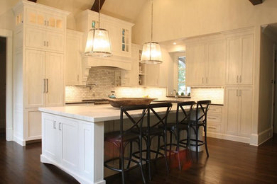 Inredning av ett klassiskt mellanstort vit vitt kök, med en undermonterad diskho, luckor med infälld panel, vita skåp, marmorbänkskiva, vitt stänkskydd, stänkskydd i marmor, rostfria vitvaror, mörkt trägolv, en köksö och brunt golv