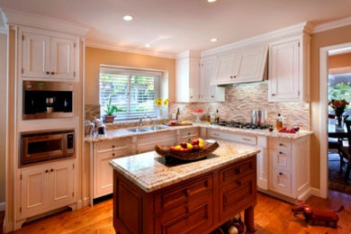 Inspiration for a mid-sized timeless u-shaped medium tone wood floor eat-in kitchen remodel in San Francisco with a double-bowl sink, beaded inset cabinets, white cabinets, multicolored backsplash, paneled appliances, an island and granite countertops