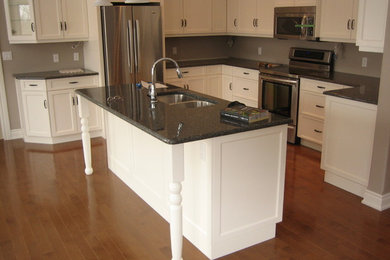 Mittelgroße Moderne Wohnküche in L-Form mit Doppelwaschbecken, Schrankfronten mit vertiefter Füllung, weißen Schränken, Granit-Arbeitsplatte, Küchengeräten aus Edelstahl, braunem Holzboden, Kücheninsel und braunem Boden in Toronto