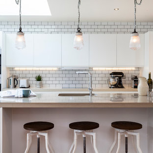 Design ideas for a transitional galley kitchen in London with an integrated sink, flat-panel cabinets, white cabinets, white splashback, subway tile splashback and with island.