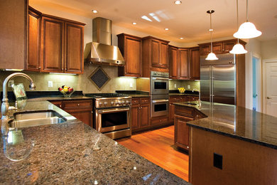 Example of a classic medium tone wood floor kitchen design in DC Metro with a double-bowl sink, medium tone wood cabinets, granite countertops, stainless steel appliances and an island