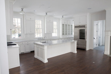 Large elegant u-shaped dark wood floor and brown floor enclosed kitchen photo in New York with an island, an undermount sink, white cabinets, marble countertops, window backsplash and stainless steel appliances