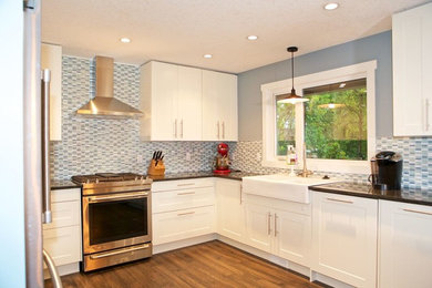 Medium sized traditional u-shaped enclosed kitchen in Calgary with a submerged sink, shaker cabinets, white cabinets, composite countertops, blue splashback, matchstick tiled splashback, stainless steel appliances, medium hardwood flooring, no island and brown floors.