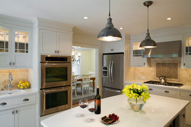 Example of a trendy enclosed kitchen design in Baltimore with an undermount sink, glass-front cabinets, stone tile backsplash, stainless steel appliances, white cabinets and beige backsplash