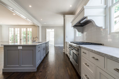 Bild på ett stort kök, med en undermonterad diskho, luckor med infälld panel, vita skåp, marmorbänkskiva, vitt stänkskydd, stänkskydd i tunnelbanekakel, rostfria vitvaror, mörkt trägolv och en köksö